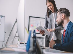 Data analyst using digital tablet near colleague at table with computers